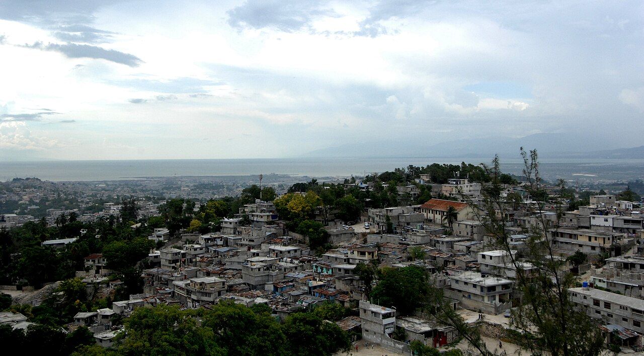 Aerial view of hillside neighborhoods in Port-au-Prince, Haiti, overlooking the bay under a cloudy sky.